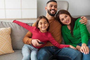 Üç kişilik mutlu bir Arap ailesi oturma odasındaki bir kanepede rahatça oturur televizyon seyreder ve birlikte güzel vakit geçirirler. Baba gülümseme paylaşırken kumandayı tutar..