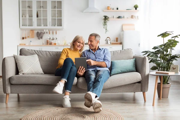 Mutlu bir son sınıf çifti modern oturma odasındaki rahat bir koltuğa oturur. Birlikte bir tablete bakıyorlar, ışık ve aydınlık bir atmosferde birbirlerine eşlik ederek eğleniyorlar..