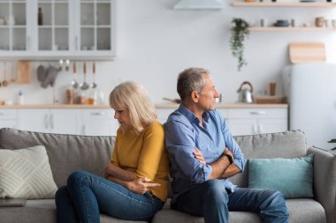 Bir çift, modern bir oturma odasındaki koltukta sırt sırta otururlar, her biri kollarını kavuşturup, sakin bir akşamda gerginlik ve anlaşmazlık belirtileri gösterirler..