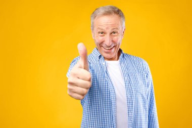 Bir adam gülümser ve olumlu bir hareketle parmağını kaldırır. O, sarı bir arkaplan önünde bir anın tadını çıkarıyor. Yüzünde mutluluk ve bağlılık ifadesi var..