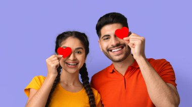 Neşeli bir çift mor bir arka fonun önünde konumlanıyor. Gözlerinin üzerinde kırmızı kalp kesikleri var, oyuncu bir sevgi göstergesi olarak. Parlak giysileri neşe katıyor.