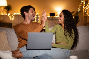 Mutlu bir çift kanepelerinde birlikte dizüstü bilgisayar kullanarak oturur. Bir kutlama anlarını paylaşıyorlar, akşamları çevrimiçi bir oyun oynarken birbirlerine beşlik çakıyorlar..