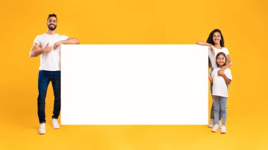 Mutlu bir aile, elinde kocaman boş bir poster olan canlı sarı bir arkaplan karşısında duruyor. Gülümsüyorlar ve birlikte yaratıcı bir girişime hazırlar..