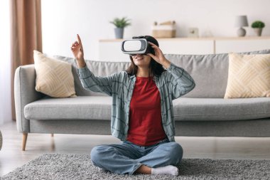 Bin yıllık Arap bir kadın oturma odasında yerde oturuyor ve sanal gerçeklik gözlüğü takıyor. İnteraktif bir video oyunuyla meşgul, yeni dünyaları keşfediyor ve gülümsüyor..