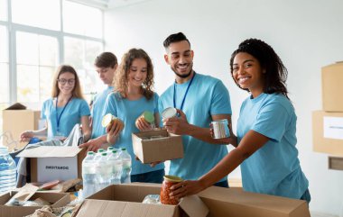 Çeşitli gönüllülerden oluşan bir grup, bir hayır kurumunda bağışlanan yiyecekleri sıralarken gülümsüyor. İhtiyaçları olanlar için gerekli malzemelerle dolu kutular hazırlıyorlar..