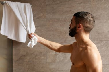 Yakışıklı genç bir Arap erkek modern bir banyoda duruyor, sıcak duştan sonra havluya uzanıyor. O kurumaya hazırlanırken, su damlacıkları kaslı vücudunda parlıyor..