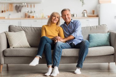 Neşeli bir son sınıf çifti rahat bir koltukta yan yana oturur. Güneşli, modern bir oturma odasında, doğal ışık ve yumuşak dekorasyonla eğlenirler..