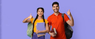 İki mutlu öğrenci parlak bir mor arka plan önünde birlikte dururlar. Gülümsüyorlar ve başparmaklarını kaldırıyorlar, ellerinde kitap tutuyorlar ve sırt çantaları takıyorlar..