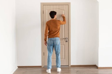 Sıradan bir genç adam ahşap bir kapının önünde duruyor, nazikçe çalıyor. İçeri girmeye hevesli görünüyor, rahat bir tarz sergiliyor kot pantolon ve süveter ile. Ayarları basit ve misafirperver..