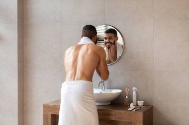 Kendine güvenen genç bir adam şık bir banyoda havluya sarılı duruyor. Yüzünü yıkarken aynaya bakar ve sakalına dokunur. Sabah rutinini gülümseyerek kucaklar..