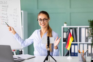 Dost canlısı bir bayan öğretmen, uzak öğrencilerle iletişim kurmak için akıllı telefonunu kullanarak Almanca dersi veriyor..