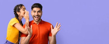 İki arkadaş neşeli bir an yaşar, biri diğerine heyecanlı görünen bir fısıltıyla. Neşeli ifadeleri, renkli bir ortamda eğlenceli bir bağlantı olduğunu gösteriyor..