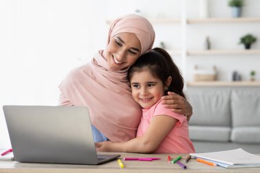 Bir anne ve küçük kızı sıcak bir anı paylaşıyor, masada dizüstü bilgisayarla uğraşırken birbirlerine yakın oturuyorlar. Yaratıcılıkla dolu aydınlık ve neşeli bir gün..