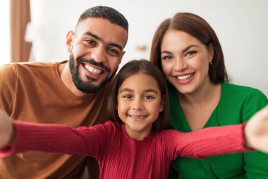 Neşeli bir aile evde selfie çekerken neşeli bir anı yakalıyor. Aileler ve kızları, sevgilerini ve bağlantılarını göstererek gülümsüyorlar..