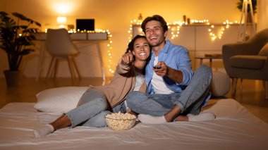 Milenyum çifti yatak odalarında film izlerken eğleniyor. Rahatlar ve bir kase patlamış mısırla rahat bir yatakta otururken TV ekranını gösterirler..
