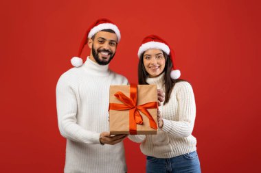 İki neşeli Arap eş, güzel paketlenmiş bir Noel hediyesi kutusunu tutarken gülümsüyor..