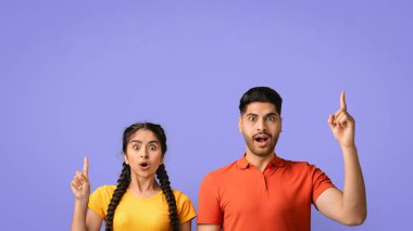 İki arkadaş, şaşkınlık ve sevinç göstererek yukarıya doğru işaret ettiklerinde heyecanlarını ifade ederler. Canlı ifadeleri, canlı mor bir arkaplan karşısında eğlenceli bir anı yakalıyor..