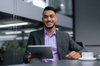 Modern ofis ortamında bir adam masada oturuyor. Bir tablet tutuyor ve takım elbise giyerken gülümsüyor. Masanın üzerine bir fincan konur..