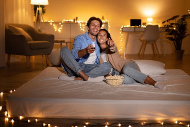 Eşler evde patlamış mısırla bir yatakta oturarak rahat bir film gecesinin tadını çıkarırlar. Yumuşak ışıklarla çevrili kanalları değiştirmek için uzaktan kumanda kullanıyorlar..