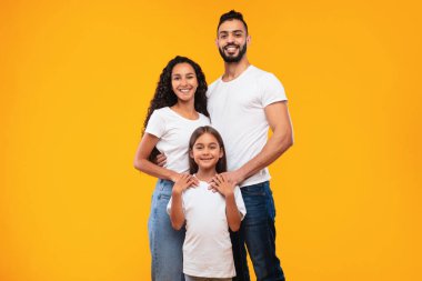 Üç aile ferdi, parlak sarı bir zemin üzerinde mutluluk saçan bir araya geldiler. Çocuk ellerini tutarken ebeveynler sıcak bir şekilde gülümsüyor ve birlik hissi yaratıyor..