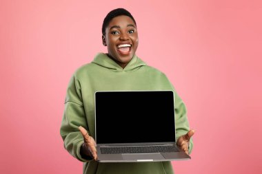 Kısa saçlı bir kişi boş bir ekranla dizüstü bilgisayarını tutarken geniş bir şekilde gülümser. Arka plan canlı bir pembe, sahnenin neşesini arttırıyor..