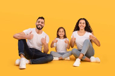 Canlı sarı bir stüdyoda yerde oturan neşeli bir aile. Geniş bir gülümseme sergiliyorlar, neşeli ve pozitif bir atmosfer yaratıyorlar..