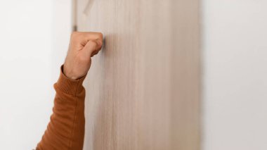 Genç adam ahşap bir kapıda duruyor, yumruğuyla nazikçe vuruyor, içeri girme hevesini gösteriyor. Sahne, bir cevap beklerken bir beklenti anı yakalıyor..