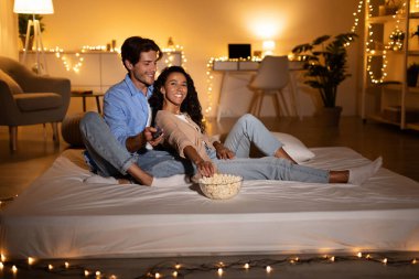 Milenyum çifti, rahat bir oturma odasında rahat bir şekilde oturup patlamış mısırın tadını çıkarıyor ve televizyonda film seyrediyor..