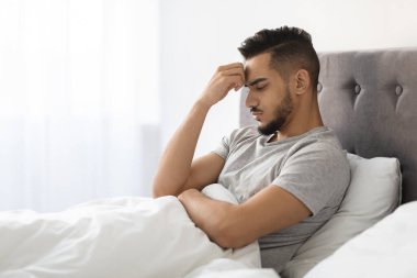 Genç bir Arap adam dalgın bir ifadeyle yatağında oturuyor. Alnını elinde dinlendiriyor, mücadeleleri hakkında derin düşünceler içinde. Odanın yumuşak doğal ışığı var, yansıma havasını arttırıyor..