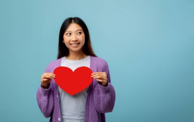 Genç bir kadın mavi bir arkaplanda duruyor, büyük kırmızı bir kalple gülümsüyor. Onun mor süveteri neşeli ana hoş bir dokunuş katıyor..