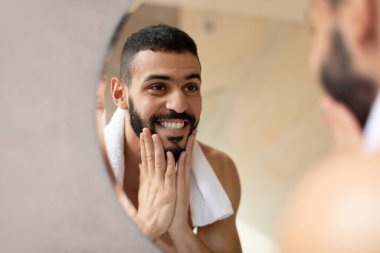 Kendine güvenen genç bir Arap aynadaki yansımasına bakarken yüzünü yıkıyor. Sakalına dokunuyor, kendini zinde ve şık bir banyo düzeninde güne hazır hissediyor..