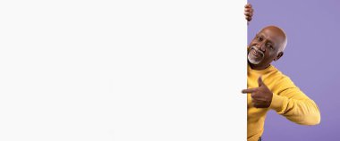 Gri saçlı ve sakallı bir adam mor bir duvarın karşısında duruyor. Sarı bir süveter giyer ve yanındaki boşluğu göstererek gülümser. Bu da dikkat çekmeye çalıştığını gösterir..