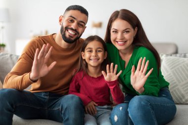 Üç kişilik neşeli Orta Doğulu aile evdeki bir kanepede oturup kameraya gülümserken ellerini mutlu bir şekilde sallıyorlar. Videodaki keyifli anlardan hoşlanırlar..