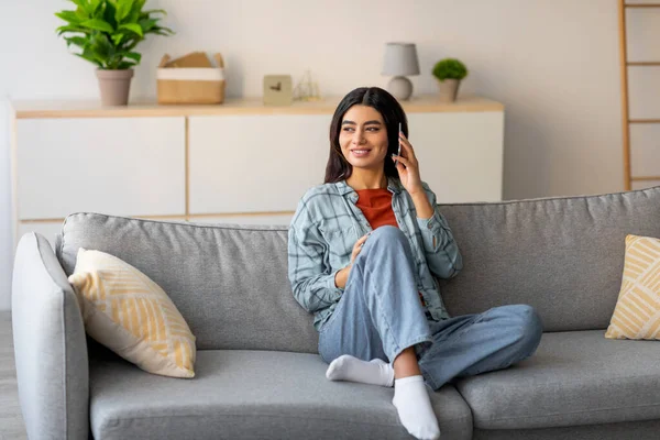 Genç bir Arap kadın evdeki rahat bir kanepede oturuyor. O gülümsüyor ve akıllı telefonuyla dostça bir sohbete daldı. Parlak ve cezbedici alan onun neşeli tavırlarına katkı yapıyor..