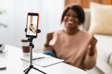 Bir kadın video görüşmesi sırasında sevinç ve heyecan ifade eder, kutlama için yumruklarını kaldırır. Parlak bir odada oturuyordu. Elinde akıllı bir telefon vardı..