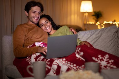 Bir çift, dizüstü bilgisayarlarında Noel filmi izlerken koltuklarında oturup birbirlerine sarılıyorlar. Bayram mevsiminin sıcağının tadını çıkararak şenlikli bir battaniyeye sarılıyorlar..