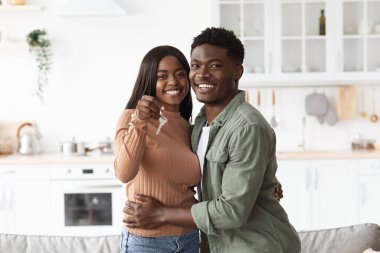 Mutlu genç siyah bir çift gururla yeni evlerinin anahtarlarını gösteriyor. Birbirlerine sımsıkı sarılıyorlar, yüzlerine gülüyorlar, ilk ev alışverişlerini birlikte kutluyorlar, parlak bir mutfakta..