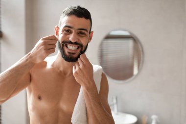 Genç bir Arap banyoda diş ipi kullanıyor. O, dişlerine odaklanırken kameraya güvenle bakıyor. Bu sağlıklı rutin, oral tedavinin önemini vurgular..