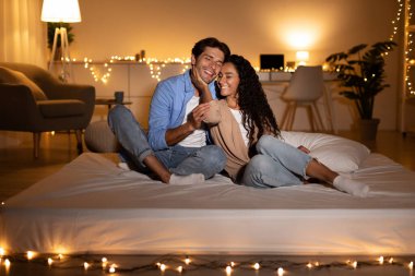 Çift bir yatakta mutlu bir şekilde oturur, birbirlerine sevgiyle sarılırlar. Kadın derin duygularını ifade ederek nazikçe kocasının yüzüne dokunur. Sıcak akşam atmosferi bağlarına sıcaklık katıyor..