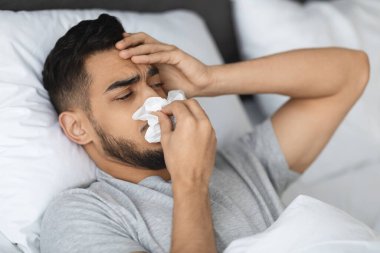 Orta Doğulu genç bir adam mevsimsel grip yüzünden kendini iyi hissetmiyor. Evde rahatsızlık ve hastalık belirtileri gösteren akıcı burnunu bir mendile sümkürdü..