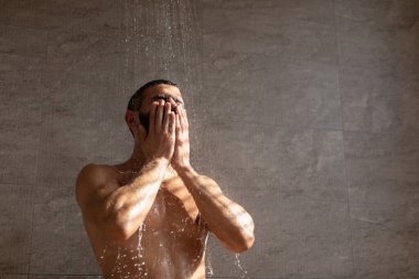 Kaslı sakallı adam yüzünü parlak bir banyoda sıcak suyun altında yıkar. Yumuşak ışık ve düşen damlacıklar vücut bakımını geliştirir ve sakin bir atmosfer yaratır..