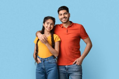 Genç bir adam ve kadın yan yana durur, mutlu bir şekilde gülümserler. Turuncu tişörtlü adamla sıradan kıyafetler giyiyorlar ve sarı bluzlu kadın neşeli bir an sergiliyor..