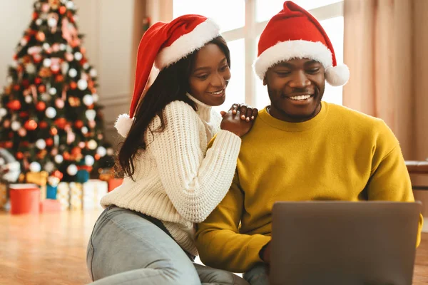 Bir çift süslü bir Noel ağacının önünde yerde oturuyor. İkisi de Noel Baba şapkası takıyor. Bir dizüstü bilgisayara bakıp gülümsüyorlar. Evlerinde şenlikli zamanlar geçiriyorlar..