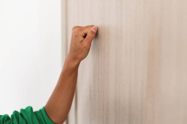 Ahşap kapıyı çalan genç bir kadının yakın görüntüsü. Girmek için hazır duruyor, düz arkaplana doğru odaklanmış bir şekilde elini vurguluyor..