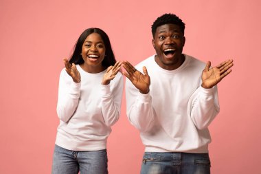 İki siyah milenyum pembe arka planda şaşkınlık ve neşe ifade ediyor. Ellerini kaldırıyorlar ve şaşkınlık içinde gülümsüyorlar. Bu paylaşılan mutluluk ve bağın bir anını yakalar..