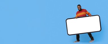 Neşeli bir ifadeye sahip bir adam parlak mavi bir arka plana karşı duruyor, elinde büyük boş bir işaret var. Renkli çizgili bir kazak ve kot pantolon giyiyor. Mesajı paylaşmaya hazır..