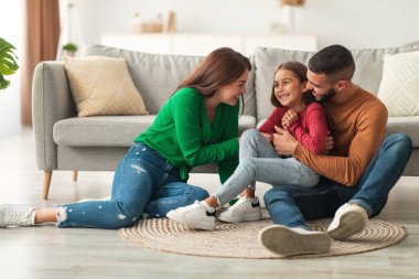 Neşeli Arap anne babalar neşeli bir şekilde gülen kızlarını oturma odasındaki halının üstünde gıdıklıyor ve aile zamanlarında neşeli anılar yaratıyorlar..