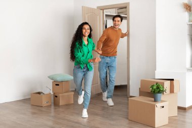 Mutlu genç çift yeni evlerine giriyor, gülümsüyor ve el ele tutuşuyorlar. Kutularla çevrili olarak, modern bir mekanda birlikte yeni bir hayata başlamanın heyecanı hoşlarına gidiyor..