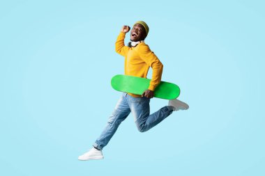 Kaykaylı, kablosuz kulaklıklı ve mavi kulaklıklı neşeli Afro-Afrikalı Amerikalı hippi. Aktif yaşam tarzının, uzunluğunun, kopyalama alanının tadını çıkarıyor.