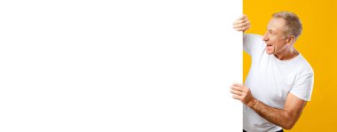 Bir adam elinde boş bir boşluk tutarken gülümsüyor. Hafifçe sola eğiliyor ve neşeli bir ifadesi var. Arka plan parlak sarı..